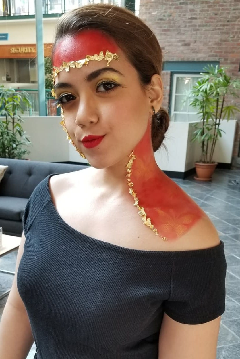 Avant-garde red and gold leaf face art with a graphic gold eye and red lip