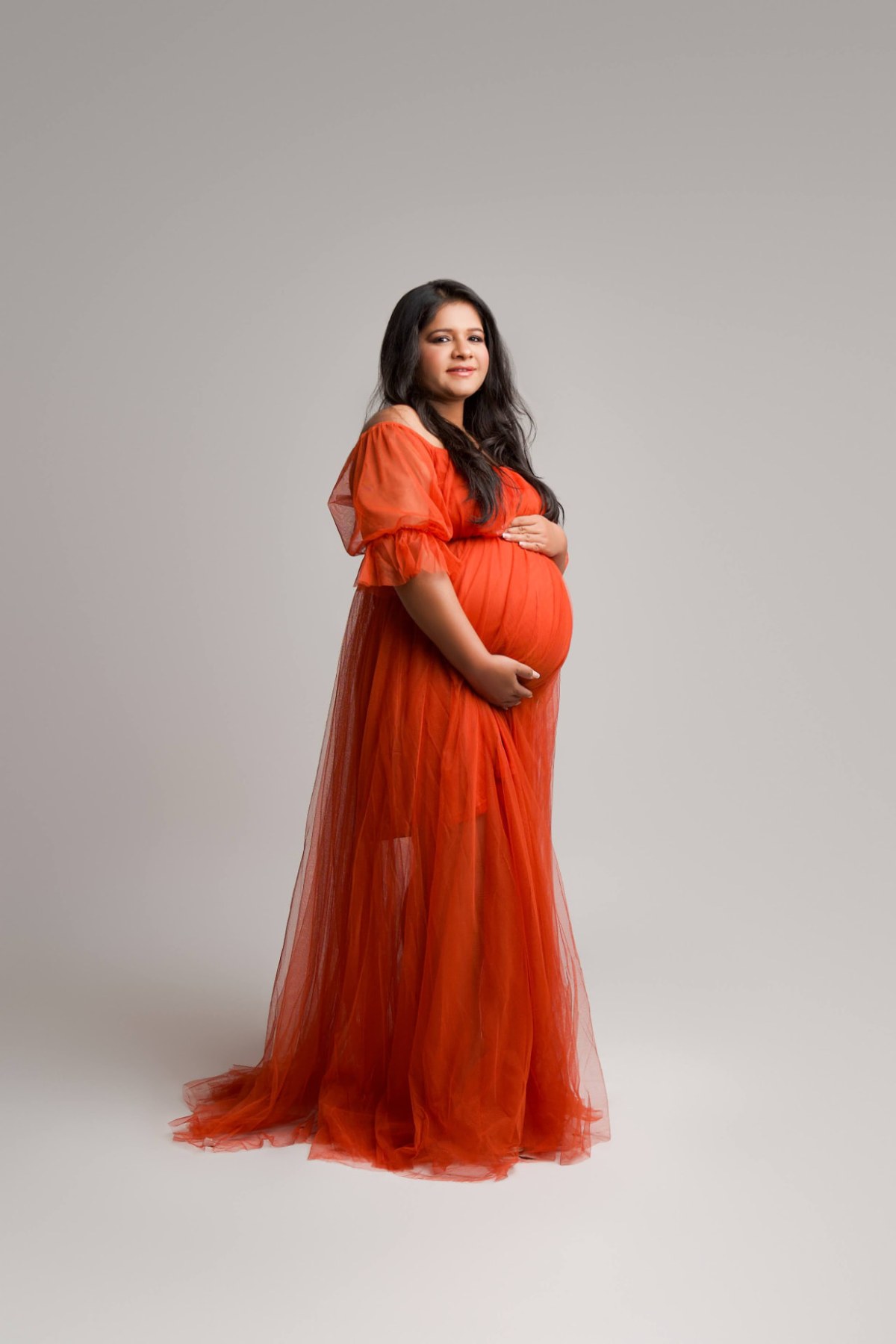 Maternity studio session makeup with luminous base, soft smoky eyes and a nude lip in a red tulle gown