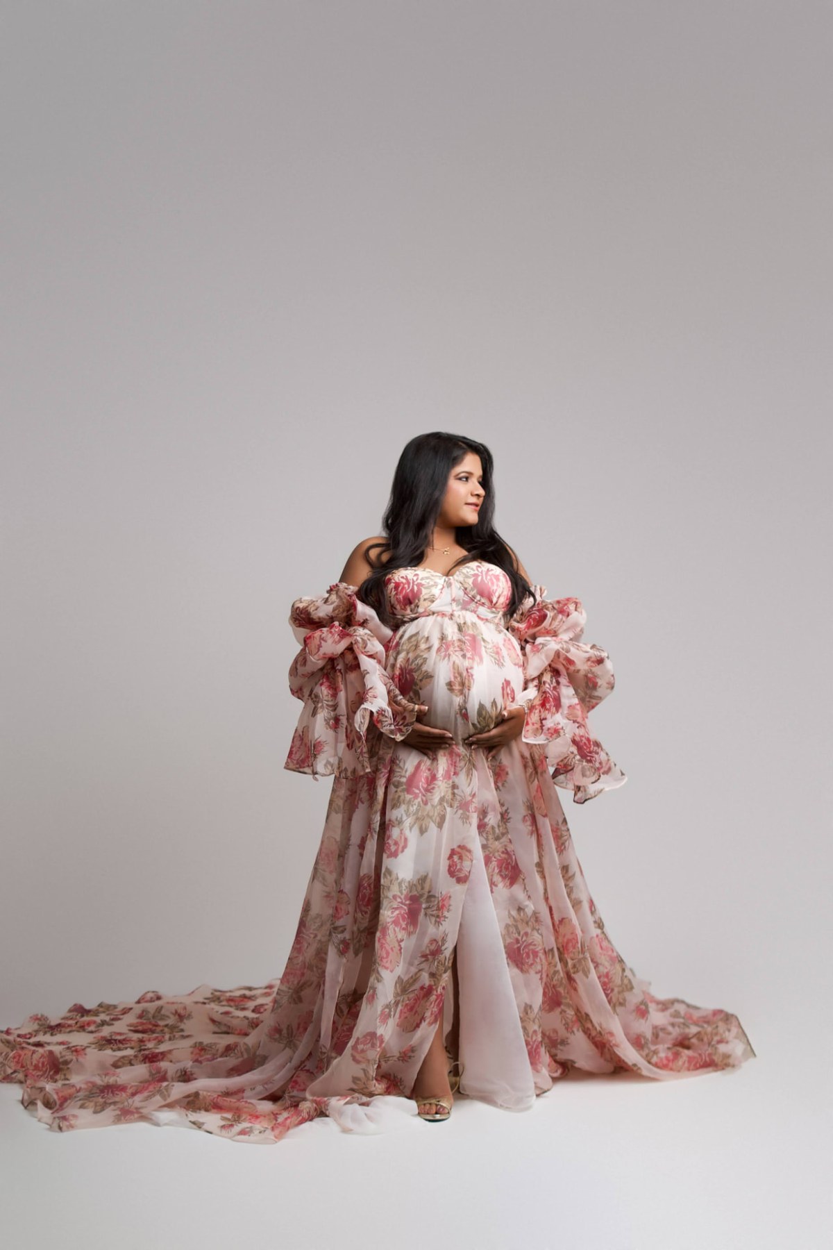 Maternity studio portrait with soft glowing skin, warm neutral eyes and a rose lip in a floral gown