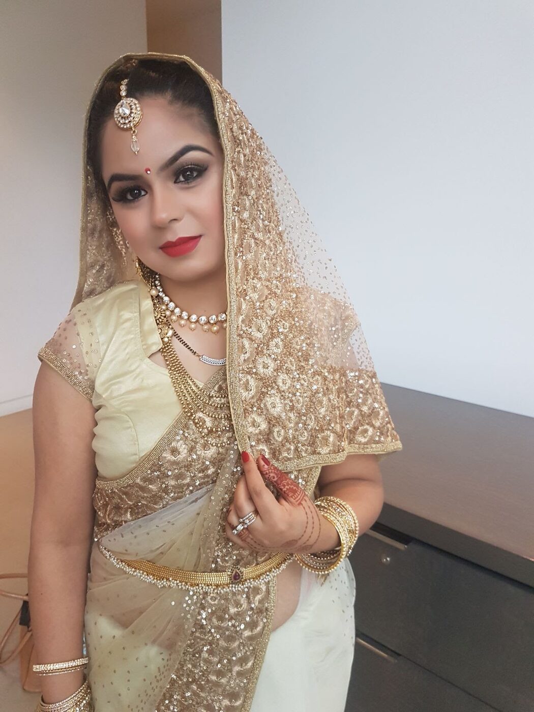 Bride in a champagne and gold saree with luminous skin and a classic red lip