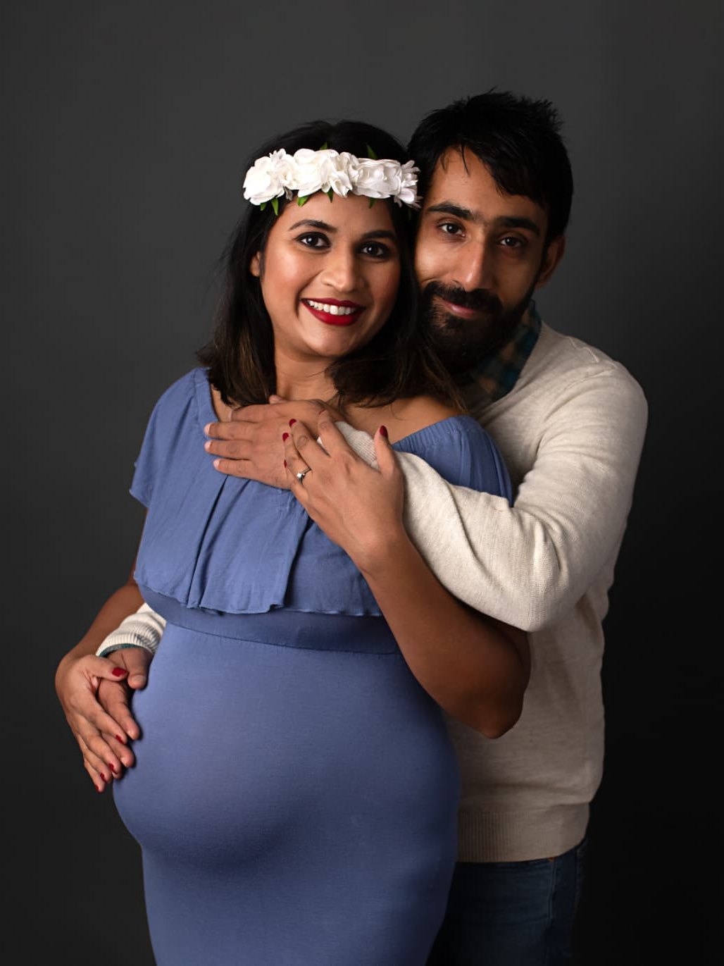 Maternity couple studio portrait with luminous skin, defined eyes and a bright red lip with a floral crown