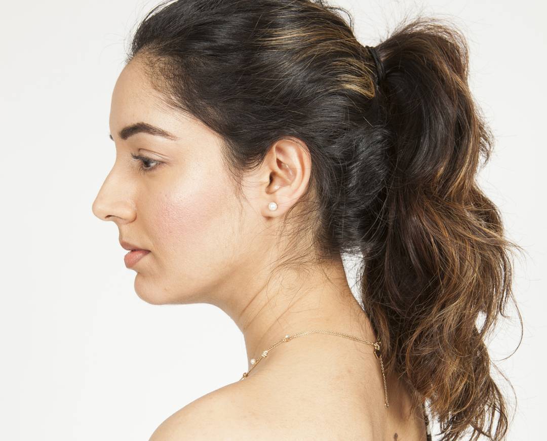 Side profile editorial studio portrait with luminous skin, groomed brows and a soft ponytail