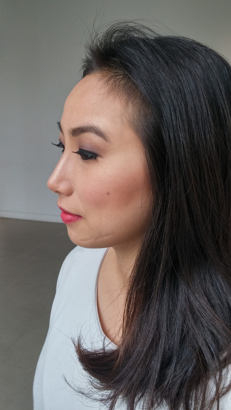 Profile view of a soft glam look with plum shadow, lash extensions and dewy skin