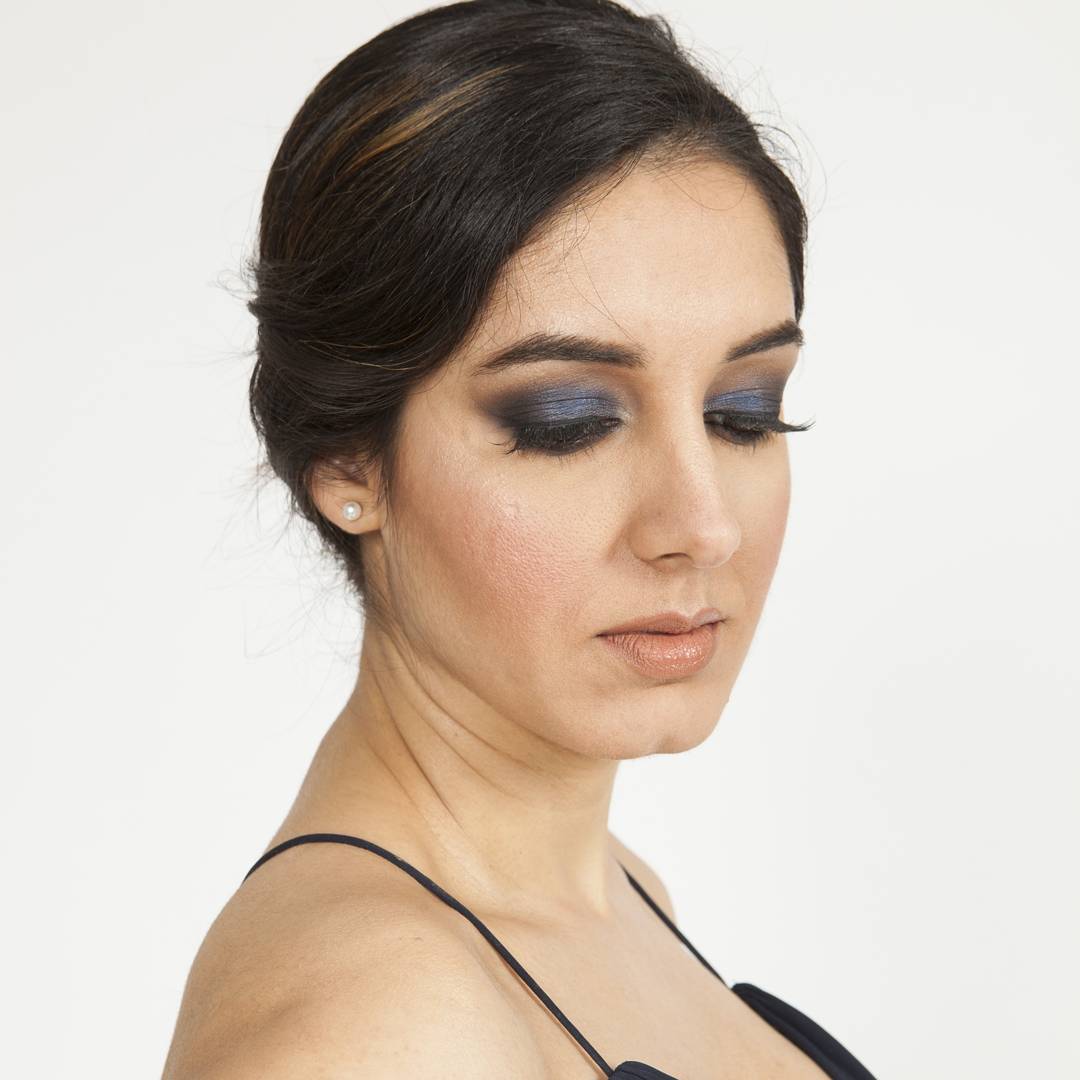 Close-up of a blue smoky eye with full lashes, glowing skin and a nude lip